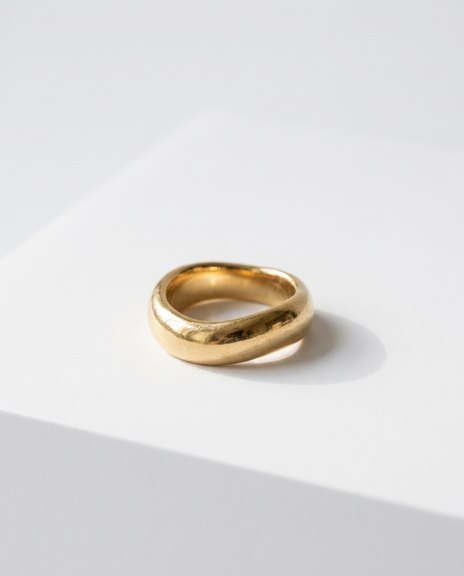 Sculptural gold ring photographed on a white stone plinth